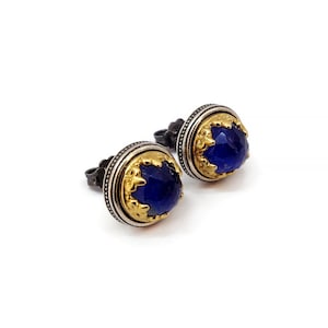 Könnte beinhalten: Ein Paar silberne Ohrstecker mit einem blauen Edelstein, der in einer goldenen Fassung sitzt. Die Ohrringe haben ein detailliertes Design um den Edelstein herum.