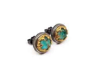 May include: A pair of stud earrings featuring round, faceted turquoise-colored stones set in gold-toned metal bezels with decorative filigree edges, surrounded by dark, oxidized silver-toned circular frames with a beaded texture.