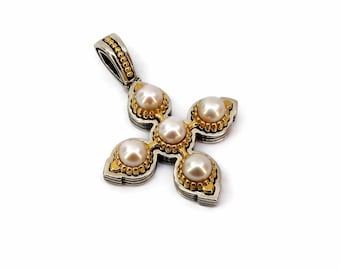 May include: A cross-shaped pendant crafted from silver and gold-toned metal, featuring five round, lustrous white pearls set in the centre and at each of the four points. The metalwork includes a textured, beaded border detail.