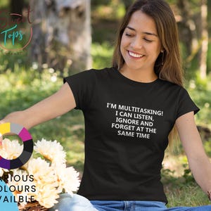 Può includere: T-shirt nero con la scritta bianca "I'M MULTITASKING! I CAN LISTEN, IGNORE AND FORGET AT THE SAME TIME". Una ruota dei colori mostra vari colori disponibili.