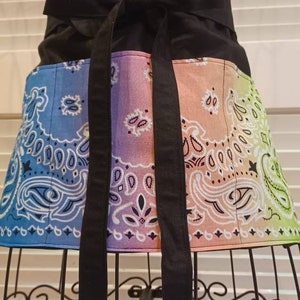 May include: A black apron with a tie waist and three pockets. The pockets are lined with a colorful paisley print in shades of blue, purple, pink, and green.