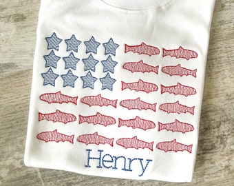 May include: White t-shirt with an embroidered American flag design featuring red fish and blue stars. The name "Henry" is embroidered below the flag.