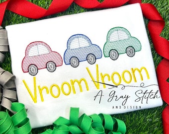Puede incluir: Una camiseta blanca con tres coches bordados en rojo, azul y verde. El texto "Vroom Vroom A Gray Stitch and Design" está bordado en amarillo.