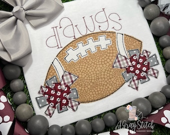 May include: White t-shirt with the word "Dawgs" embroidered in maroon thread. A brown and white football with maroon and white pom-poms is embroidered below the word.