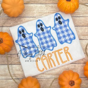 May include: White onesie with three blue and white gingham ghost appliques and the name "Carter" embroidered in orange thread.
