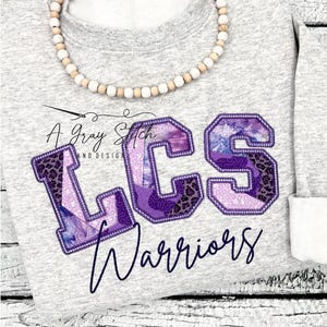 May include: Purple and white patchwork letters spelling "LCS" with a black outline and a purple and white "Warriors" text below on a gray sweatshirt.