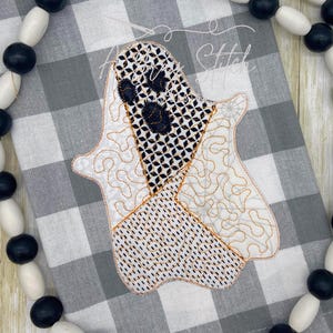 May include: A white ghost applique with black eyes and a patchwork design. The ghost is stitched with orange thread on a gray and white checkered fabric.