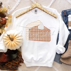 Könnte beinhalten: Weißes Sweatshirt mit einem Design aus braunen und weißen Karos in Form eines Tortenstücks. Das Tortenstück hat einen weißen Schlagsahne-Belag.