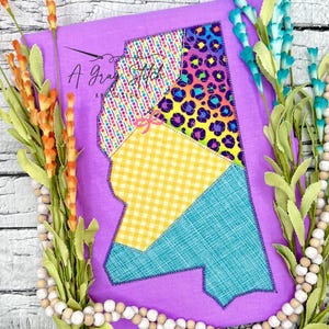 May include: Purple fabric with a patchwork design of a state outline. The patches are yellow gingham, blue, pink polka dot, and rainbow leopard print.