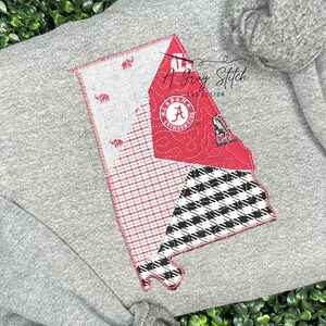 May include: A gray sweatshirt with a patchwork design in the shape of the state of Alabama. The patchwork includes red, white, and black patterns, with the text "A Gray Stitch and Design" in the upper right corner.