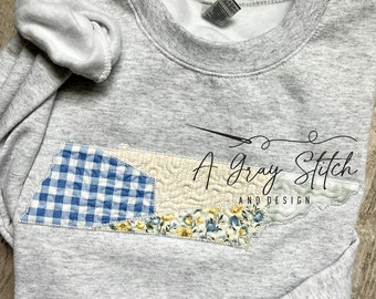 May include: A gray sweatshirt with a patchwork design of blue and yellow gingham and floral fabric in the shape of the state of Tennessee. The text "A Gray Stitch and Design" is embroidered on the sweatshirt.