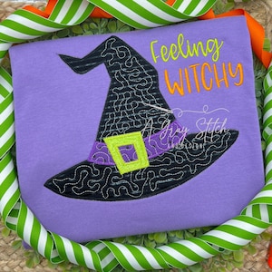 Puede incluir: Camiseta morada con un sombrero de bruja negro y el texto "Feeling Witchy" en hilo naranja y verde.