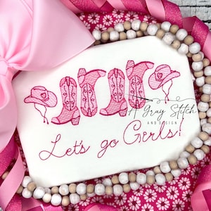 May include: Pink embroidered design on a white t-shirt with the text "Let's go Girls!" and a row of pink cowboy boots and a pink cowboy hat.