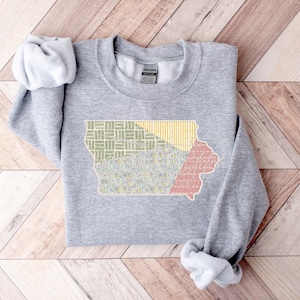 May include: A gray sweatshirt with a patchwork design of the state of Iowa in yellow, green, and pink.
