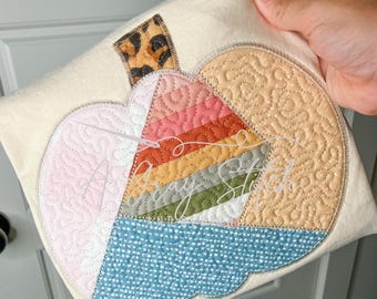 Puede incluir: Una camiseta beige con un diseño de calabaza de patchwork colorido. La calabaza está hecha de diferentes telas con varias texturas y patrones, incluyendo estampado de leopardo, rayas y lunares.