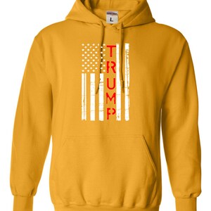 May include: A yellow hoodie with a white and red American flag design. The word "TRUMP" is written vertically in red letters down the center of the flag.