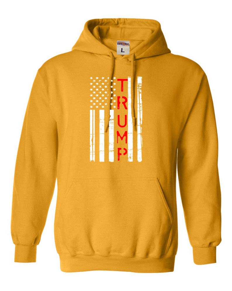 May include: A yellow hoodie with a white and red American flag design. The word "TRUMP" is written vertically in red letters down the center of the flag.