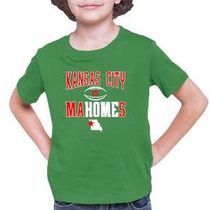 K&ouml;nnte beinhalten: Gr&uuml;nes T-Shirt mit einer wei&szlig;en Grafik, auf der "Kansas City is Mahomes" steht, mit einem Football und einem roten Stern &uuml;ber einem wei&szlig;en Umriss des Bundesstaates Missouri.