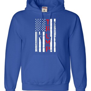 May include: A royal blue hooded sweatshirt with a white and red distressed American flag design. The word "TRUMP" is printed vertically in red on the flag.