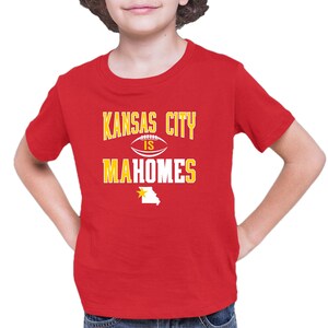 K&ouml;nnte beinhalten: Rotes T-Shirt mit kurzen &Auml;rmeln und einem wei&szlig;en Aufdruck mit der Aufschrift "Kansas City is Mahomes" mit einem Football und einem gelben Stern &uuml;ber einem wei&szlig;en Umriss des Bundesstaates Missouri.