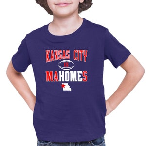 K&ouml;nnte beinhalten: Ein kurz&auml;rmliges T-Shirt in Lila mit einer wei&szlig;en Grafik, auf der "Kansas City is Mahomes" steht, mit einer wei&szlig;en Fu&szlig;ballgrafik und einem roten Stern &uuml;ber einem wei&szlig;en Umriss des Bundesstaates Missouri.