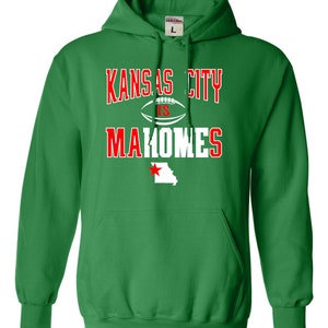 Puede incluir: Sudadera con capucha verde con el texto "Kansas City is Mahomes" en letras blancas y rojas. Un bal&oacute;n de f&uacute;tbol blanco con una estrella roja est&aacute; entre "City" e "is". Una estrella roja est&aacute; en un contorno blanco del estado de Missouri.