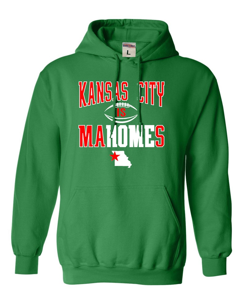 Puede incluir: Sudadera con capucha verde con el texto "Kansas City is Mahomes" en letras blancas y rojas. Un bal&oacute;n de f&uacute;tbol blanco con una estrella roja est&aacute; entre "City" e "is". Una estrella roja est&aacute; en un contorno blanco del estado de Missouri.
