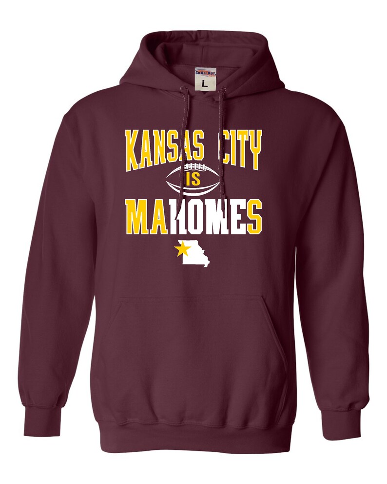 Puede incluir: Sudadera con capucha color granate con el texto "Kansas City is Mahomes" en letras blancas y amarillas. Una estrella amarilla y el contorno del estado de Misuri se encuentran debajo del texto.