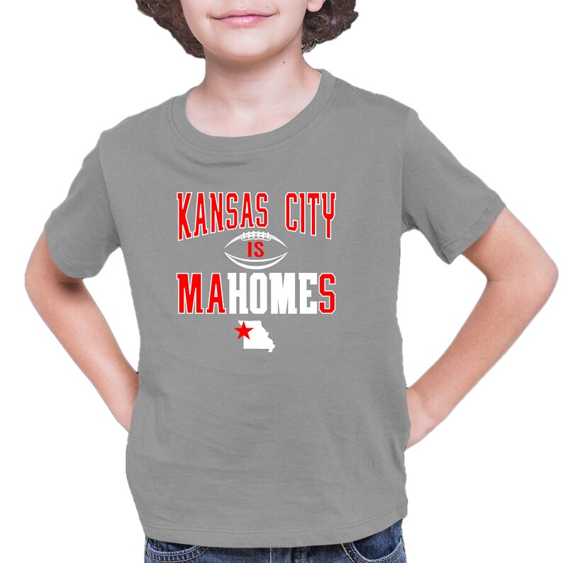 K&ouml;nnte beinhalten: Ein graues T-Shirt mit rotem Text, der "Kansas City is Mahomes" sagt, mit einer wei&szlig;en Fu&szlig;ballgrafik und einem roten Stern &uuml;ber einem wei&szlig;en Umriss des Bundesstaates Missouri.