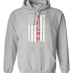 May include: A gray hooded sweatshirt with a white and red American flag design. The word "TRUMP" is printed vertically in red down the center of the flag.
