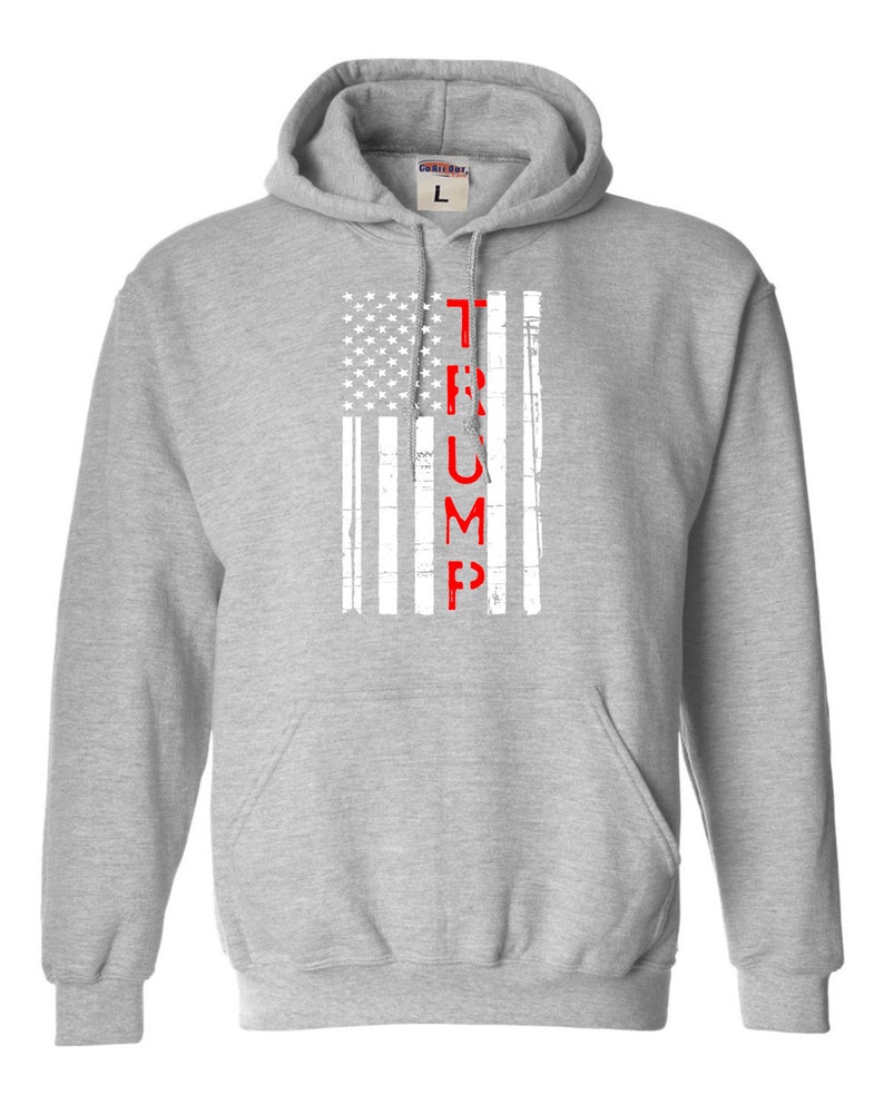 May include: A gray hooded sweatshirt with a white and red American flag design. The word "TRUMP" is printed vertically in red down the center of the flag.