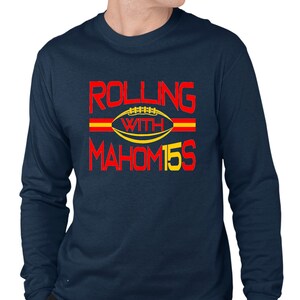 May include: Navy blue long-sleeve t-shirt with a red and yellow graphic that says "Rolling with Mahomes 15". The graphic features a football with a red and yellow stripe.