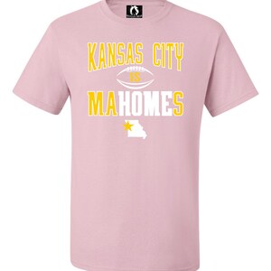 K&ouml;nnte beinhalten: Rosafarbenes T-Shirt mit einer wei&szlig;en Grafik, auf der "Kansas City is Mahomes" steht, mit einem Fu&szlig;ball und einem gelben Stern &uuml;ber dem Bundesstaat Missouri.