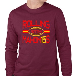 May include: A maroon long-sleeve t-shirt with the text "ROLLING WITH MAHOM15S" in red and yellow lettering. A yellow football with red laces is in the center of the text.