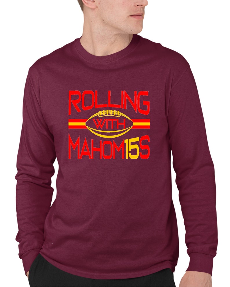 May include: A maroon long-sleeve t-shirt with the text "ROLLING WITH MAHOM15S" in red and yellow lettering. A yellow football with red laces is in the center of the text.