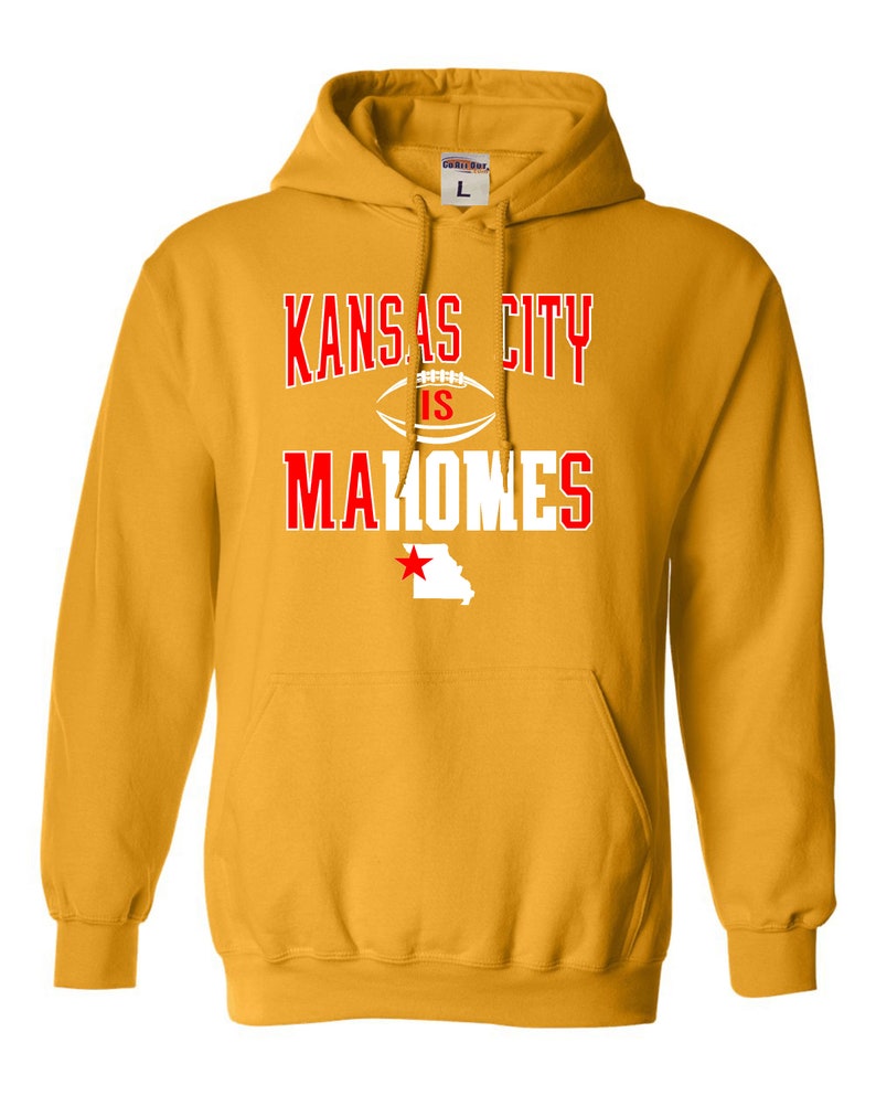 Puede incluir: Una sudadera con capucha amarilla con un gr&aacute;fico blanco que dice "Kansas City is Mahomes" en letras rojas. El gr&aacute;fico tambi&eacute;n incluye un bal&oacute;n de f&uacute;tbol y una estrella roja sobre el contorno del estado de Misuri.