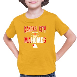 K&ouml;nnte beinhalten: Ein gelbes T-Shirt mit dem Text "Kansas City is Mahomes" in Rot und Wei&szlig;. Ein roter Stern und die Umrisse des Bundesstaates Missouri befinden sich unter dem Text.