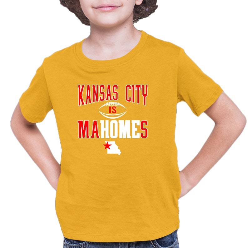 K&ouml;nnte beinhalten: Ein gelbes T-Shirt mit dem Text "Kansas City is Mahomes" in Rot und Wei&szlig;. Ein roter Stern und die Umrisse des Bundesstaates Missouri befinden sich unter dem Text.