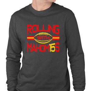 May include: A dark gray long-sleeve t-shirt with the text "ROLLING WITH MAHOM15S" in red and yellow. A yellow football with red laces is in the center of the text.