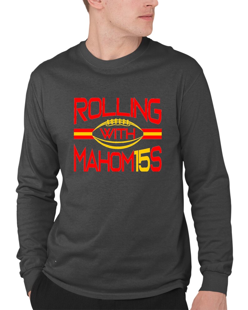May include: A dark gray long-sleeve t-shirt with the text "ROLLING WITH MAHOM15S" in red and yellow. A yellow football with red laces is in the center of the text.