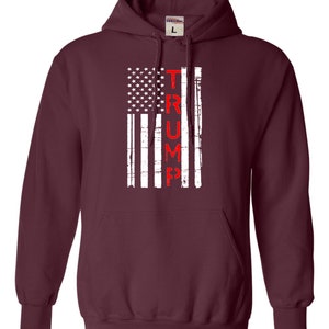 May include: A maroon hooded sweatshirt with a distressed American flag design and the word "TRUMP" printed vertically in red.