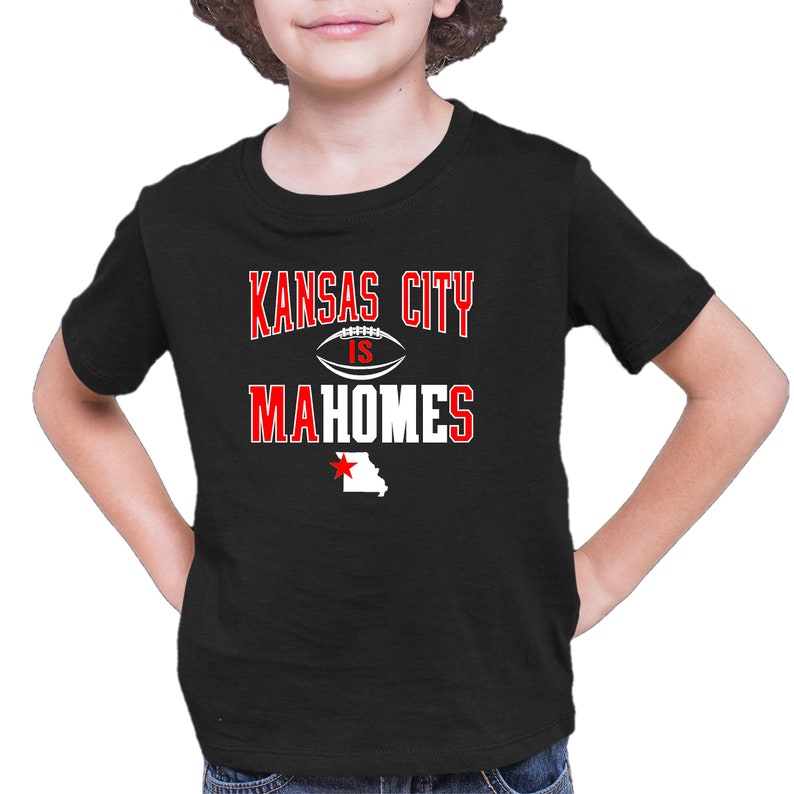 K&ouml;nnte beinhalten: Schwarzes T-Shirt mit wei&szlig;em Text, der "Kansas City is Mahomes" lautet, mit einer Football-Grafik und einem roten Stern &uuml;ber einem wei&szlig;en Umriss des Bundesstaates Missouri.