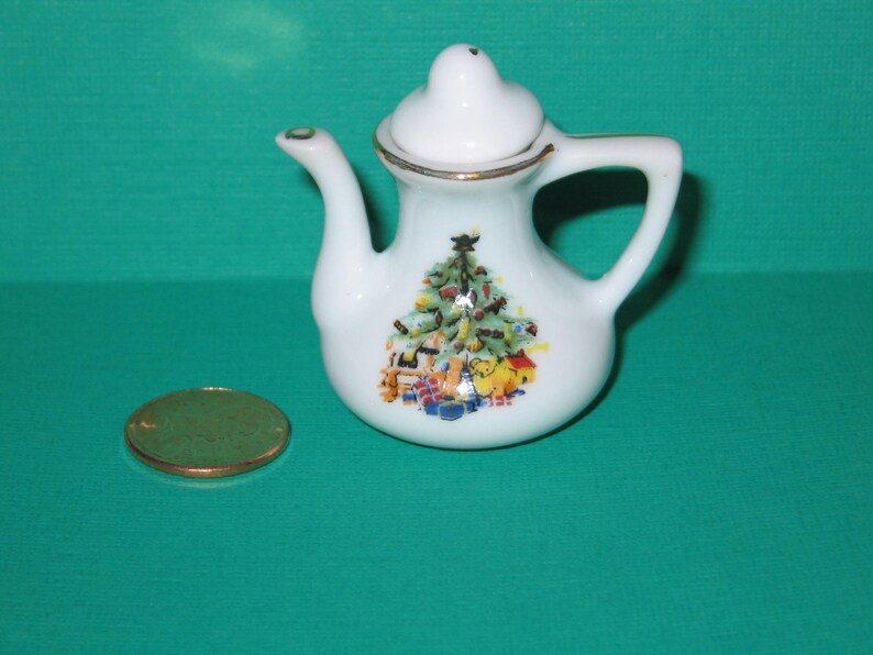 May include: White porcelain teapot with a Christmas tree design. The teapot has a gold trim and a handle. The design features a Christmas tree with presents and a star on top.