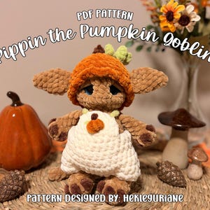 Puede incluir: Un peluche de duende tejido a ganchillo en color marrón con un gorro de calabaza naranja y un peto blanco. El texto dice PDF PATTERN Pippin the Pumpkin Goblin y PATTERN DESIGNED BY: HEKLEGURIANE. El duende tiene orejas grandes y patas marrones.