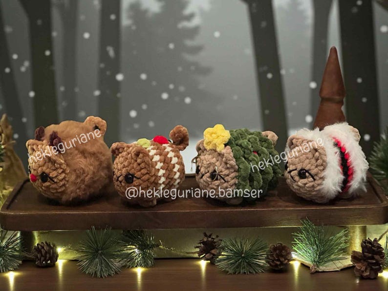 May include: Four small, round, crocheted plush figures arranged in a row. The first is brown with antlers, the second is brown with white stripes, the third is green with a yellow star, and the fourth is white and brown with a brown cone on top.