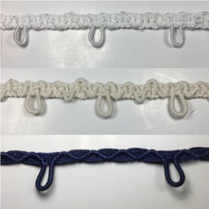 May include: Three different types of white, cream, and navy blue curtain tiebacks with loops. The tiebacks are made of a woven fabric and have a decorative design.