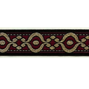Puede incluir: Un ribete burdeos y negro con un diseño estampado en oro. El ribete tiene un patrón repetitivo de remolinos y puntos.