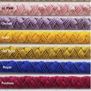 May include: A close-up of eight different colors of braided cord. The colors are natural, light pink, orchid, gold, old gold, royal blue, fuchsia, and light blue.