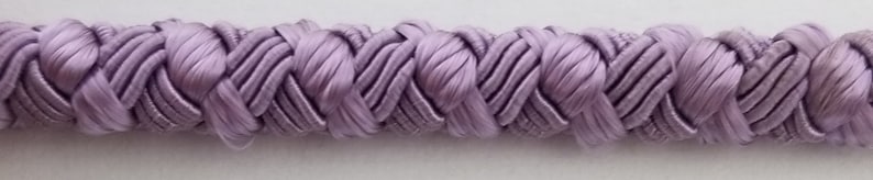 May include: A close-up of a lavender braided trim. The trim is made of a soft, silky fabric and has a delicate, intricate design.