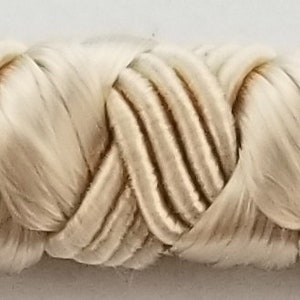 May include: A close-up of a cream-colored braided trim. The trim is made of a soft, woven fabric and has a delicate, intricate design.